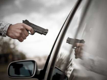 man pointing gun at car