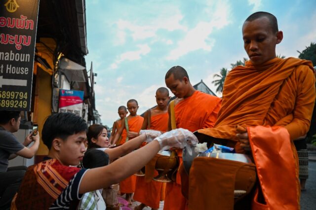 Monks have to make their way through hundreds of visitors on plastic stools offering alms