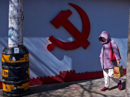 A woman walks by a Communist Party's logo on display near a residential area in Beiji