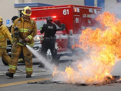 An LAFD firefighter extinguishes a small street fire during demonstrations following the d