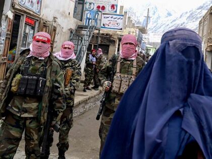 Taliban security personnel stand guard as an Afghan burqa-clad woman (R) walks along a str