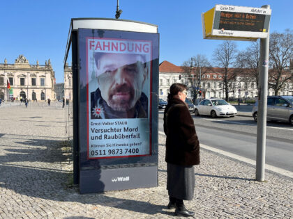 A woman waits at a bus stop with a manhunt poster by the Lower Saxony State Criminal Polic
