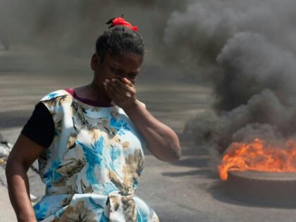 A woman walks past burning tires during a demonstration following the resignation of its P