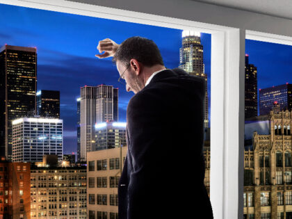 Middle aged businessman looking out a bright office window and thinking in city of LA