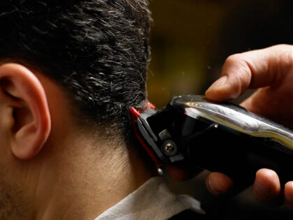 Barber cutting man's hair, close-up of electric razor, side view - stock photo