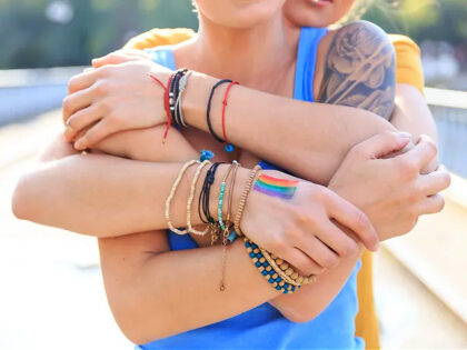 Two young girls embracing on bridge, one standing behind other. One with arm tattoo, other