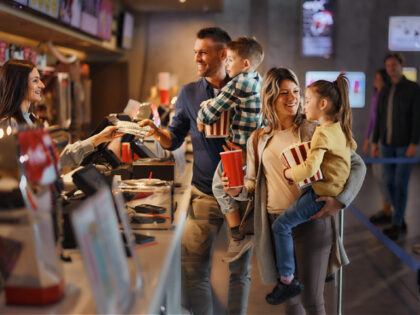 Happy parents and their kids buying movie tickets at concession stand in cinema.