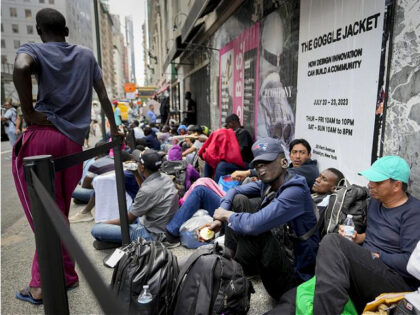 Migrants sit in a queue outside of The Roosevelt Hotel that is being used by the city as t