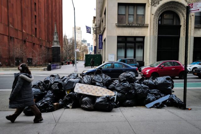 A woman walks past a pile of trash on a Manhattan street on March 19, 2024