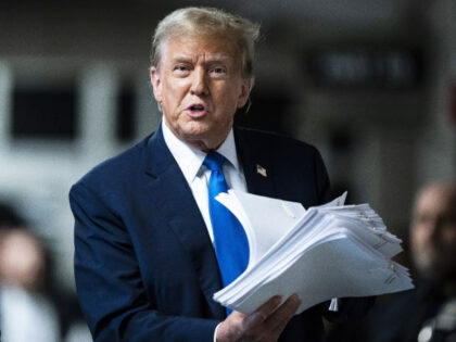 Former President Donald Trump holds printouts of news stories as he speaks to reporters at