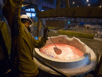 A worker prepares a crucible of molten aluminum by scrapping off the slag layer in the fou