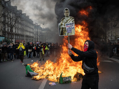 PARIS, FRANCE - MARCH 28: A protester holds a placard next to fire during a rally against