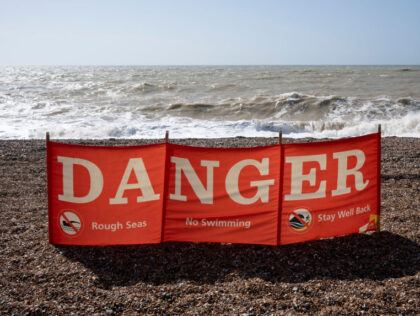 A seascape of a danger banner telling swimmers not to enter the water due to rough seas, o
