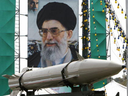 An unidentifed Iranian missile stands on display in front of a large portrait of Iran's Su