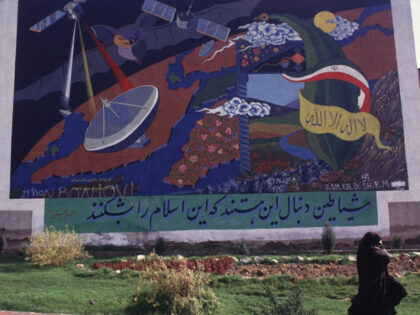 A woman in black chador passes by a huge mural depicting satellite television networks as