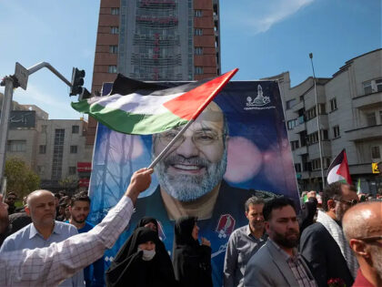 An Iranian man is waving a Palestinian flag in front of a portrait of Mohammad Reza Zahedi