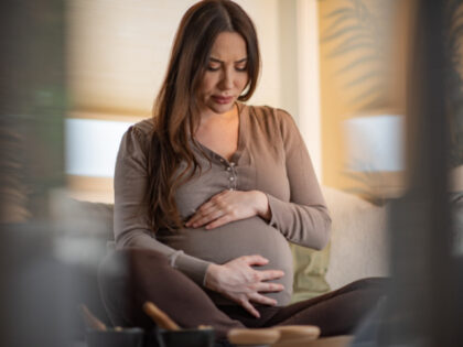 Pregnant woman feels pain while sitting on a sofa in her living room.