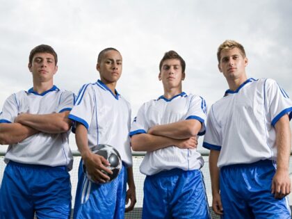 Serious-looking soccer players stand on a field and look down.