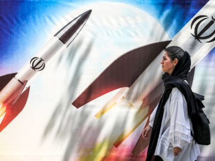 A woman walks past a banner depicting launching missiles bearing the emblem of the Islamic