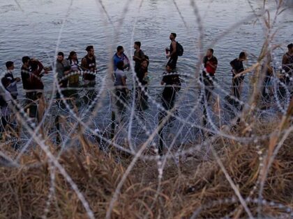 Migrants wait to climb over concertina wire after they crossed the Rio Grande and entered