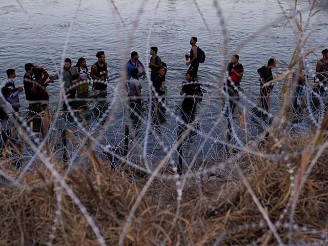 Migrants wait to climb over concertina wire after they crossed the Rio Grande and entered