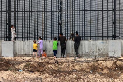 Displaced Palestinian children chat with an Egyptian soldier through the fence separating