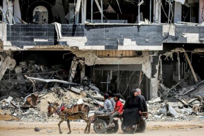 Gazans ride a donkey-drawn cart past a destroyed building in Khan Yunis