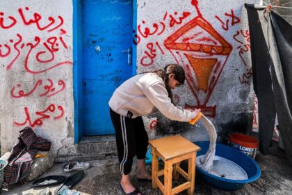 A girl washes clothes by hand at a camp for displaced Palestinians erected in a school run