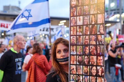 A protester with a zip over her mouth holds up photographs of the Israeli hostages at a Te
