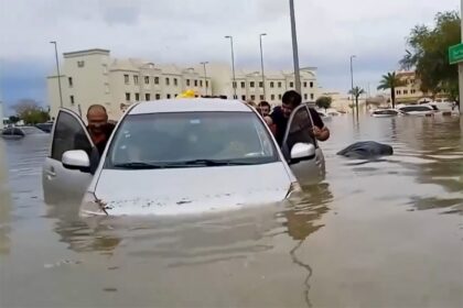 Residents push a waterlogged car along a flooded street in the desert city of Dubai after