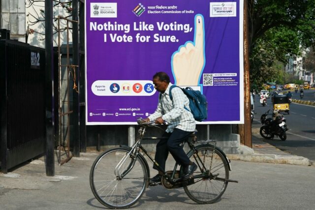 A man rides past an election awareness poster displayed on a street ahead of India’s upc