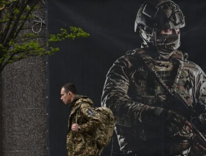 A Ukrainian serviceman walks past a recruiting poster in Kyiv on April 23, 2024
