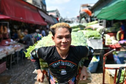 A vendor sweats as he pulls a vegetable cart at Bangkok's biggest fresh market, with peopl