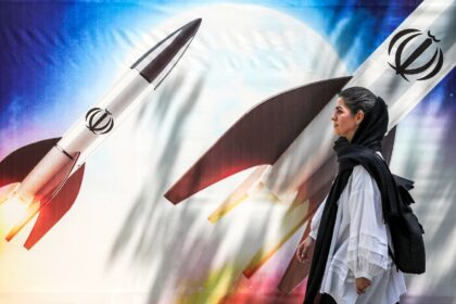 A woman walks past a banner depicting missiles bearing the emblem of the Islamic Republic
