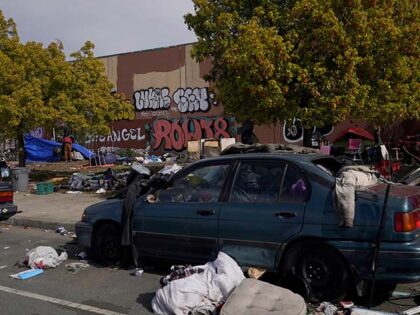 A person stands in front of a tent behind a car filled with debris at a homeless encampmen