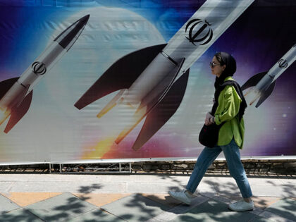 A woman walks past a banner showing missiles being launched, in northern Tehran, Iran, Fri