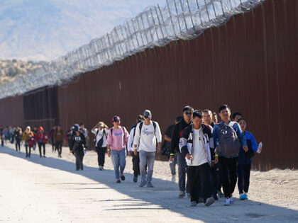 A group of people, including many from China, walk along the wall after crossing the borde