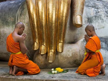 Thailand, Sukothai, Wat Si Chum, Buddhist monks praying in front of seated Buddha and gold