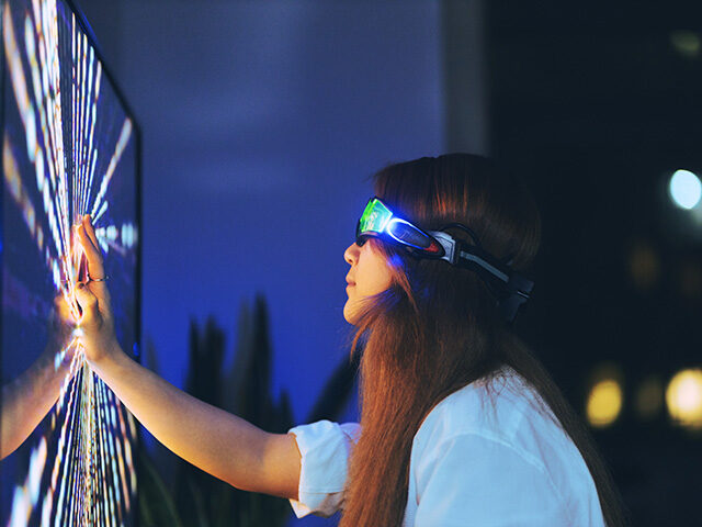 Young woman wearing augmented reality glasses touching screen with hands - stock photo