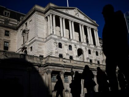 Pedestrians cross the streets in front of The Bank of England illuminated by a ray of sunl