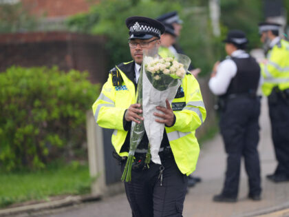 A police officer makes his way to lay flowers on the corner of Laing Close in Hainault, no