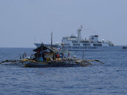 A China Coast Guard ship (R) monitors a Philippine fishing boat during the distribution of