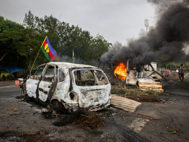 This photograph shows a Kanak flag waving next to a burning vehicle at an independantist r