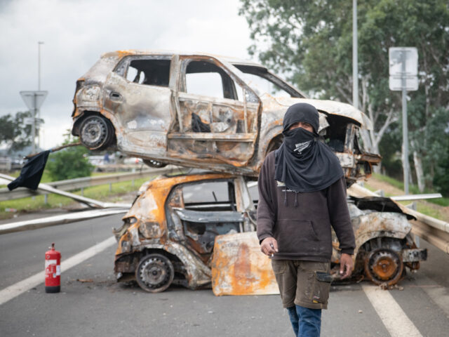 A bystander poses in front of burnt vehicles in a roadblock at the entrance to Ducos, Fran