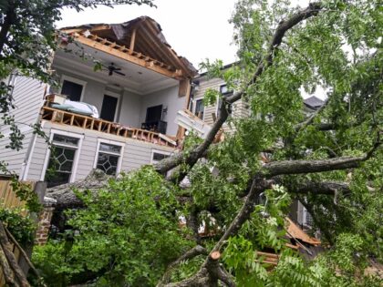 A man looks at a severely damaged home after being hit by a fallen tree from heavy winds a