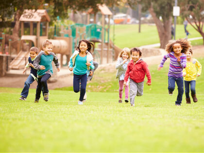 Group Of Young Children Running Towards Camera In Park Smiling