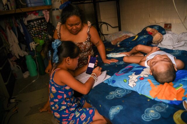 Cindella Manabat (C) helps her daughter Ella Araza (L) with homework, at their house in Ma