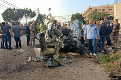 Lebanese soldiers and onlookers gather around the remnants of a car after it was hit by an