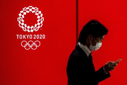 A masked man walks past a logo of the Tokyo 2020 Olympics