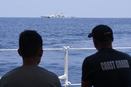 Philippine Coast Guard personnel observe a China Coast Guard ship during distribution of f